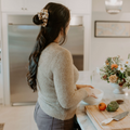Woman preparing food in a modern kitchen with a vase of flowers on the counter.