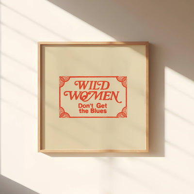 Framed artwork with text 'Wild Women Don't Get the Blues' on a wall with sunlight casting shadows.