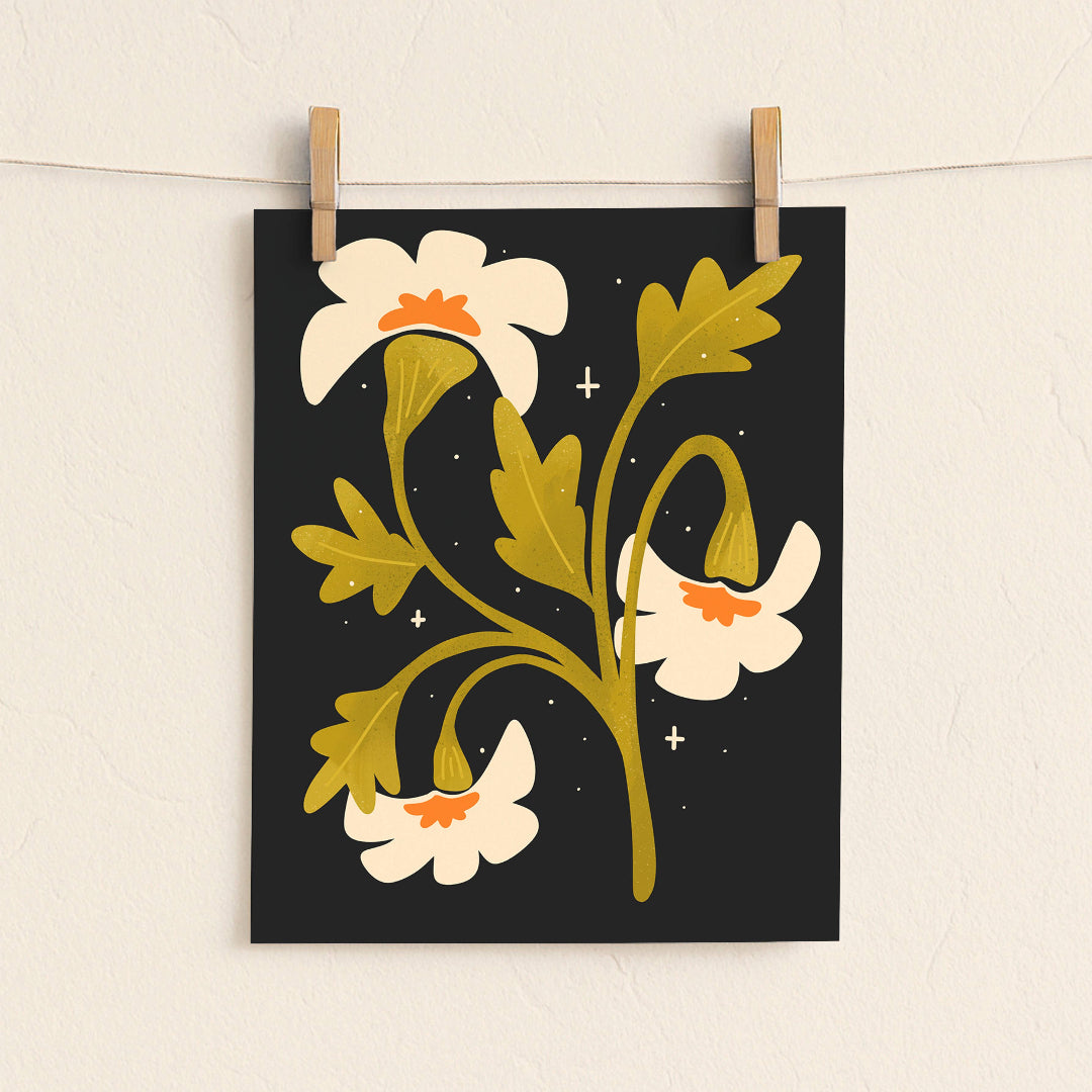A vertical art print featuring a stylized botanical illustration of cream flowers with mustard yellow leaves on a black background, hanging from two wooden clothespins on a white wall.