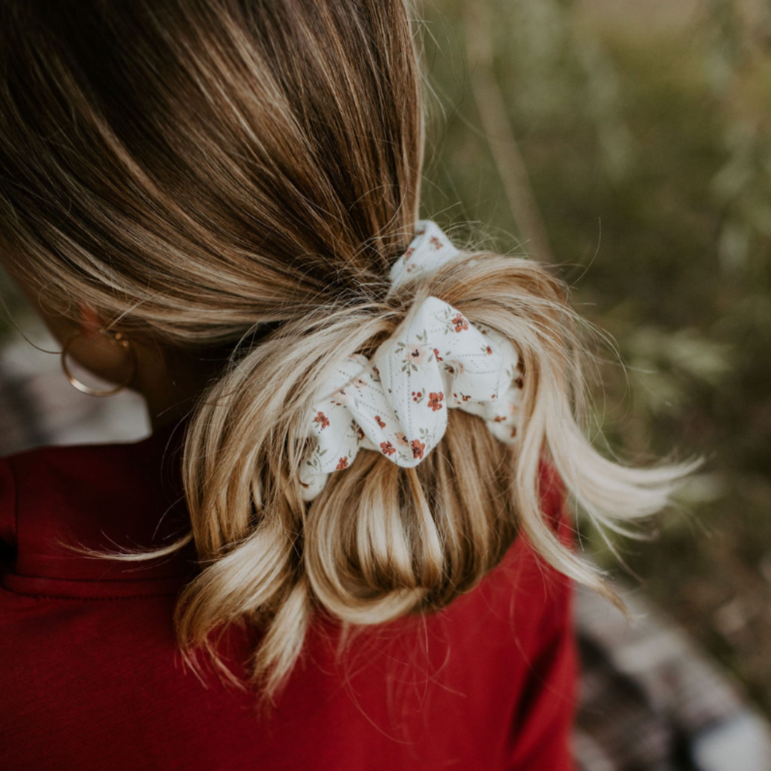 Person with blonde hair tied in a ponytail with a floral scrunchie, wearing a red top.
