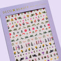 A sheet of colorful nail art stickers with various nature-themed designs. The sheet is purple and has the brand name "Deco Beauty" printed on it. There's a section titled "Wildflower" and instructions on how to apply the stickers. The stickers include designs like flowers, insects, mushrooms, and foxes.