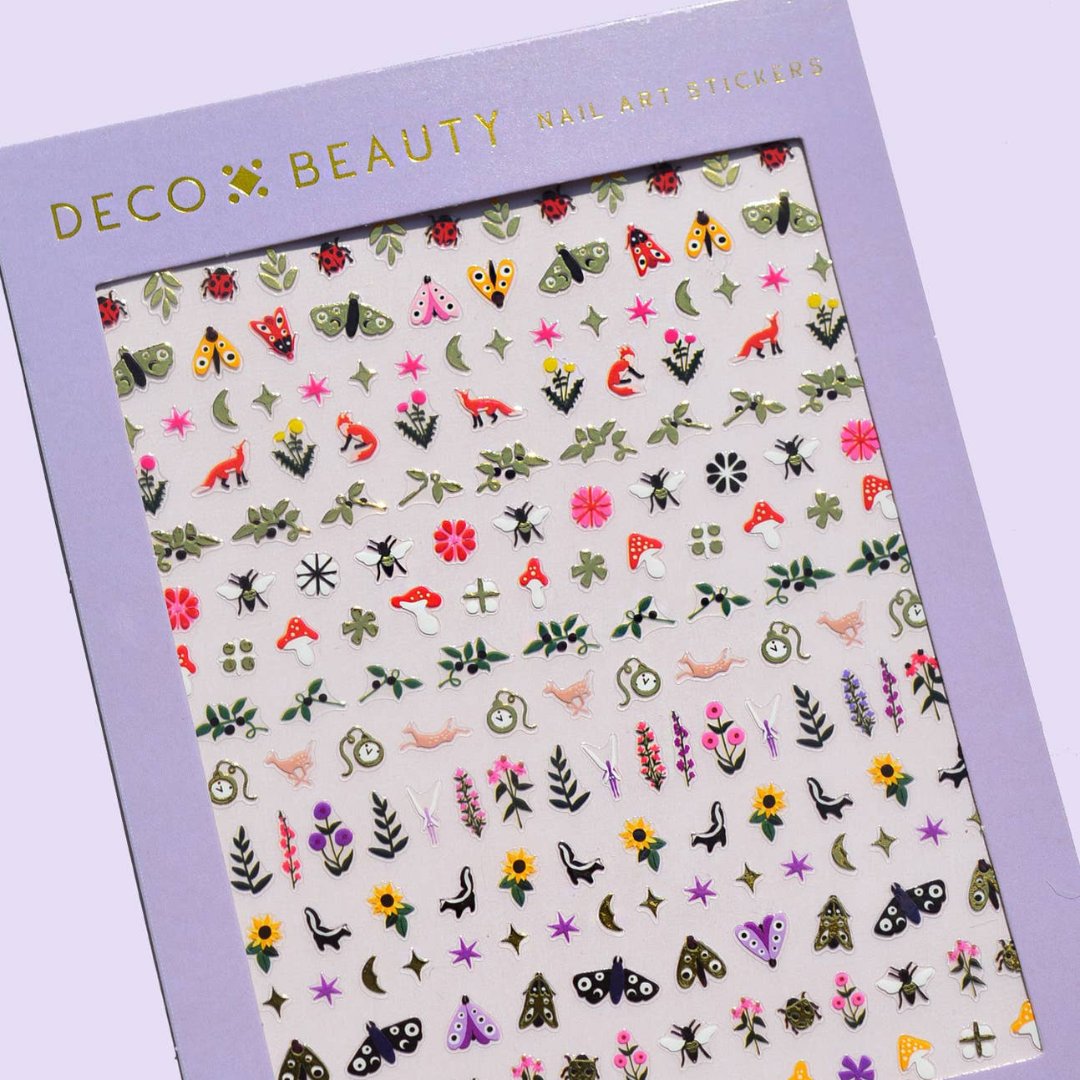 A sheet of colorful nail art stickers with various nature-themed designs. The sheet is purple and has the brand name "Deco Beauty" printed on it. There's a section titled "Wildflower" and instructions on how to apply the stickers. The stickers include designs like flowers, insects, mushrooms, and foxes.
