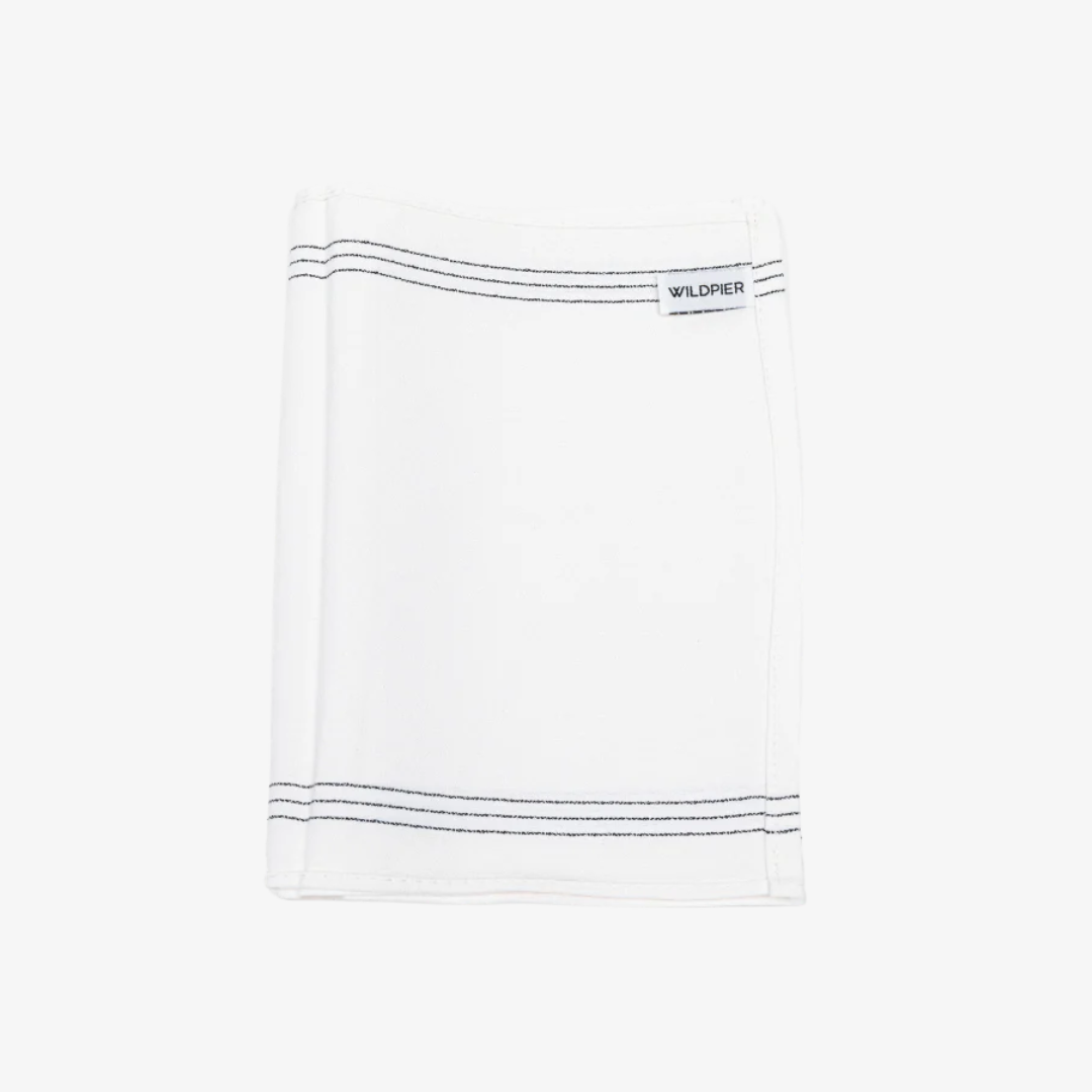 A white, textured exfoliating washcloth with three black stripes along the top edge. The washcloth has a tag with the word "WILDPIER" on it.
