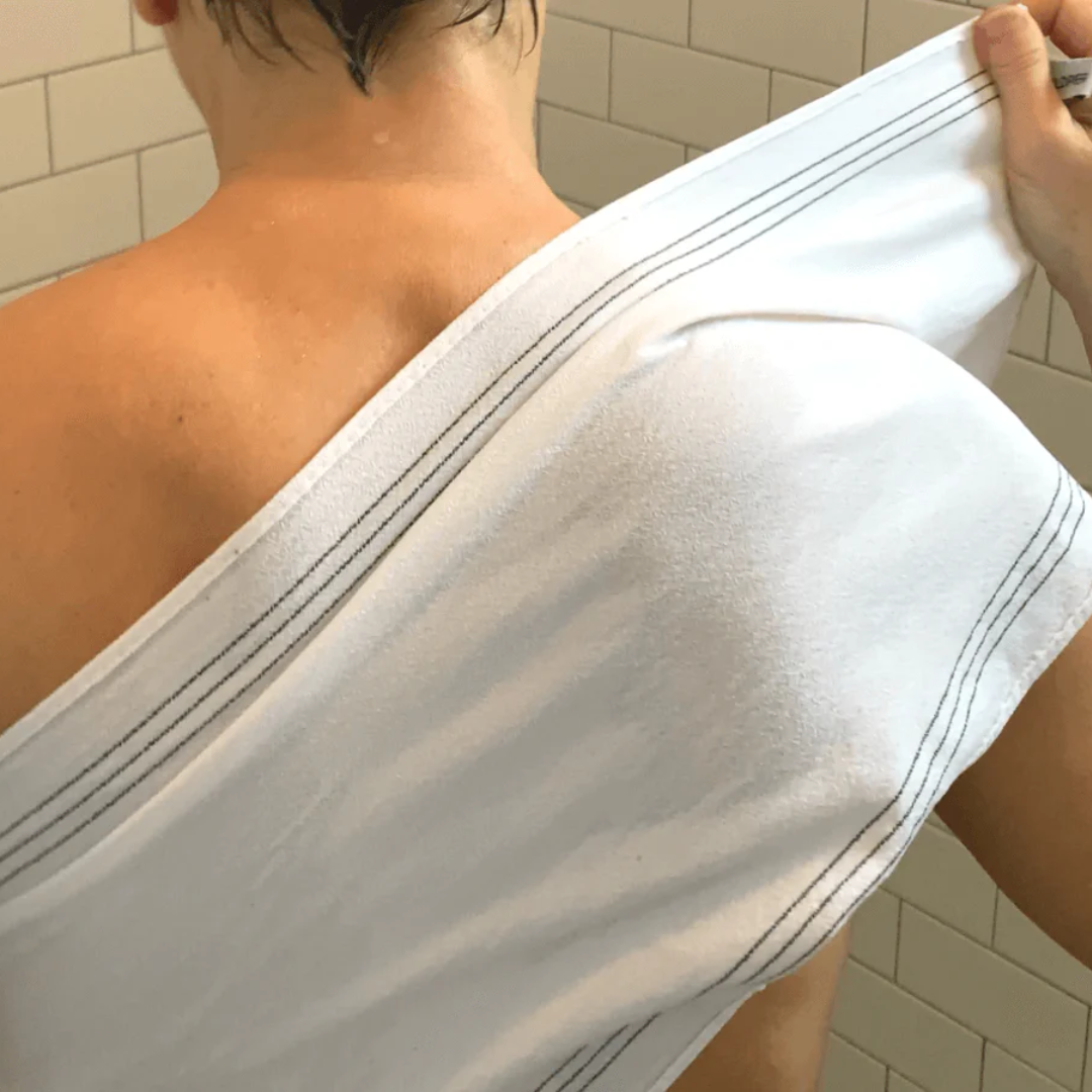 A white, textured exfoliating washcloth with three black stripes along the top edge. The washcloth has a tag with the word "WILDPIER" on it.