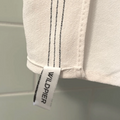 A white, textured exfoliating washcloth with three black stripes along the top edge. The washcloth has a tag with the word "WILDPIER" on it.