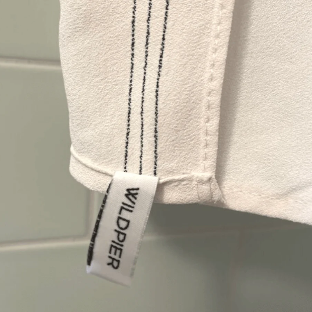 A white, textured exfoliating washcloth with three black stripes along the top edge. The washcloth has a tag with the word "WILDPIER" on it.