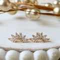 Gold leaf-shaped earrings on a textured surface with decorative elements.