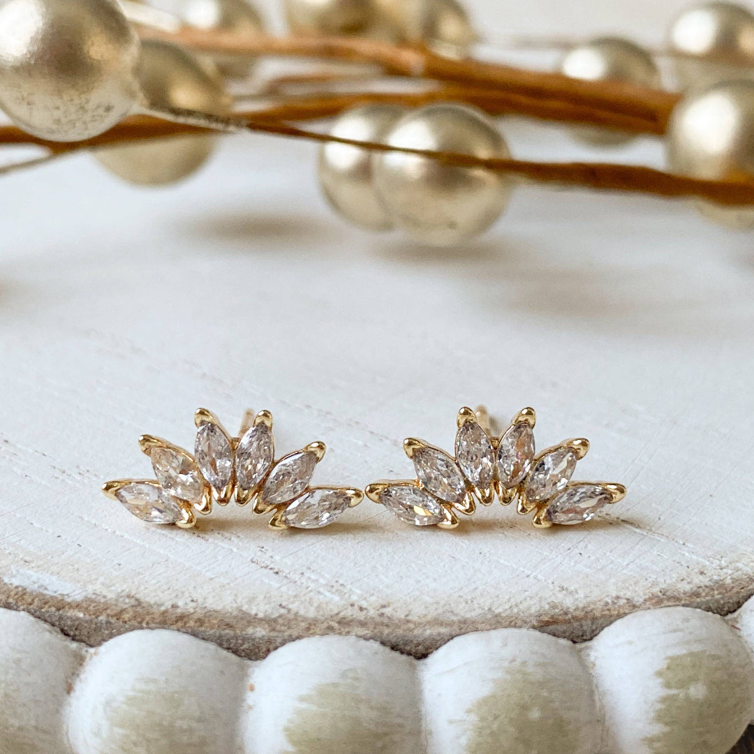 Gold leaf-shaped earrings on a textured surface with decorative elements.