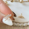 Gold earring with clear gemstones held between fingers against a blurred background