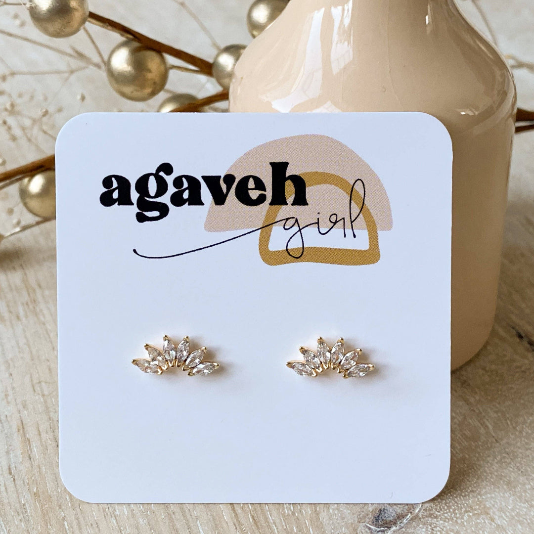 Gold earrings on a 'agaveh girl' branded card with decorative elements in the background.