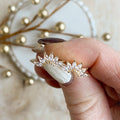 Gold ring with floral design held by a hand against a decorative background