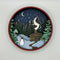 A Paint By Layers Craft Kit featuring a circular shadow box with a pre-designed winter scene. The scene depicts a cabin in a snowy forest under a starry night sky. The kit includes layers of wood, paint, and instructions. The title of the kit is 