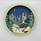 A Paint By Layers Craft Kit featuring a circular shadow box with a pre-designed winter scene. The scene depicts a cabin in a snowy forest under a starry night sky. The kit includes layers of wood, paint, and instructions. The title of the kit is 