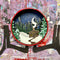 A Paint By Layers Craft Kit featuring a circular shadow box with a pre-designed winter scene. The scene depicts a cabin in a snowy forest under a starry night sky. The kit includes layers of wood, paint, and instructions. The title of the kit is 