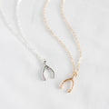 Two wishbone necklaces, one silver and one gold, on a light gray background.