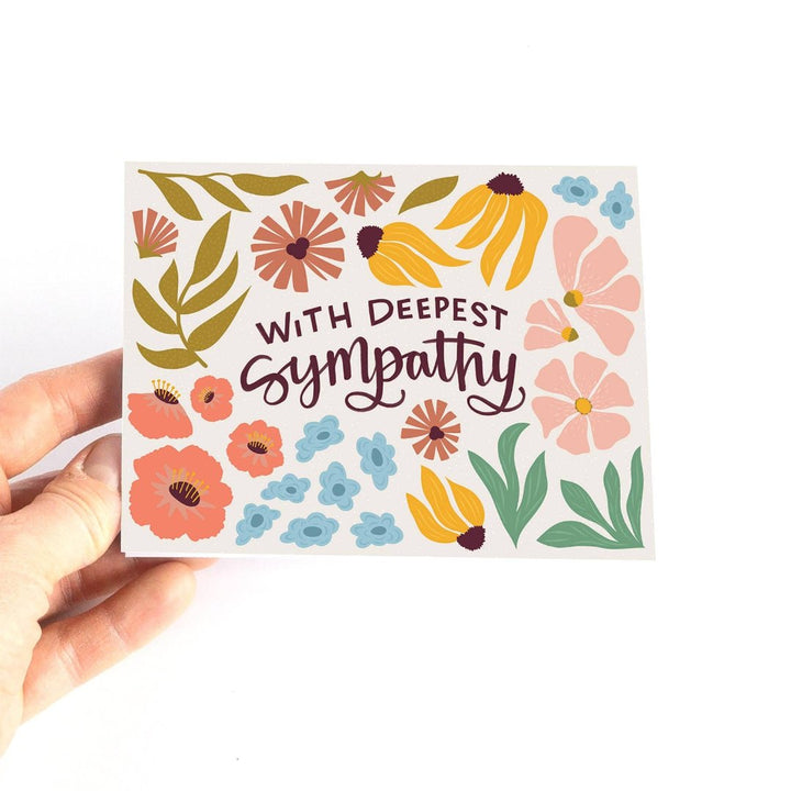 A sympathy card with a floral design. The card has a white background with colorful flowers, leaves, and the text 