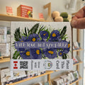 Plantable card with flowers and 'With love and sympathy' text, held in front of a store shelf.