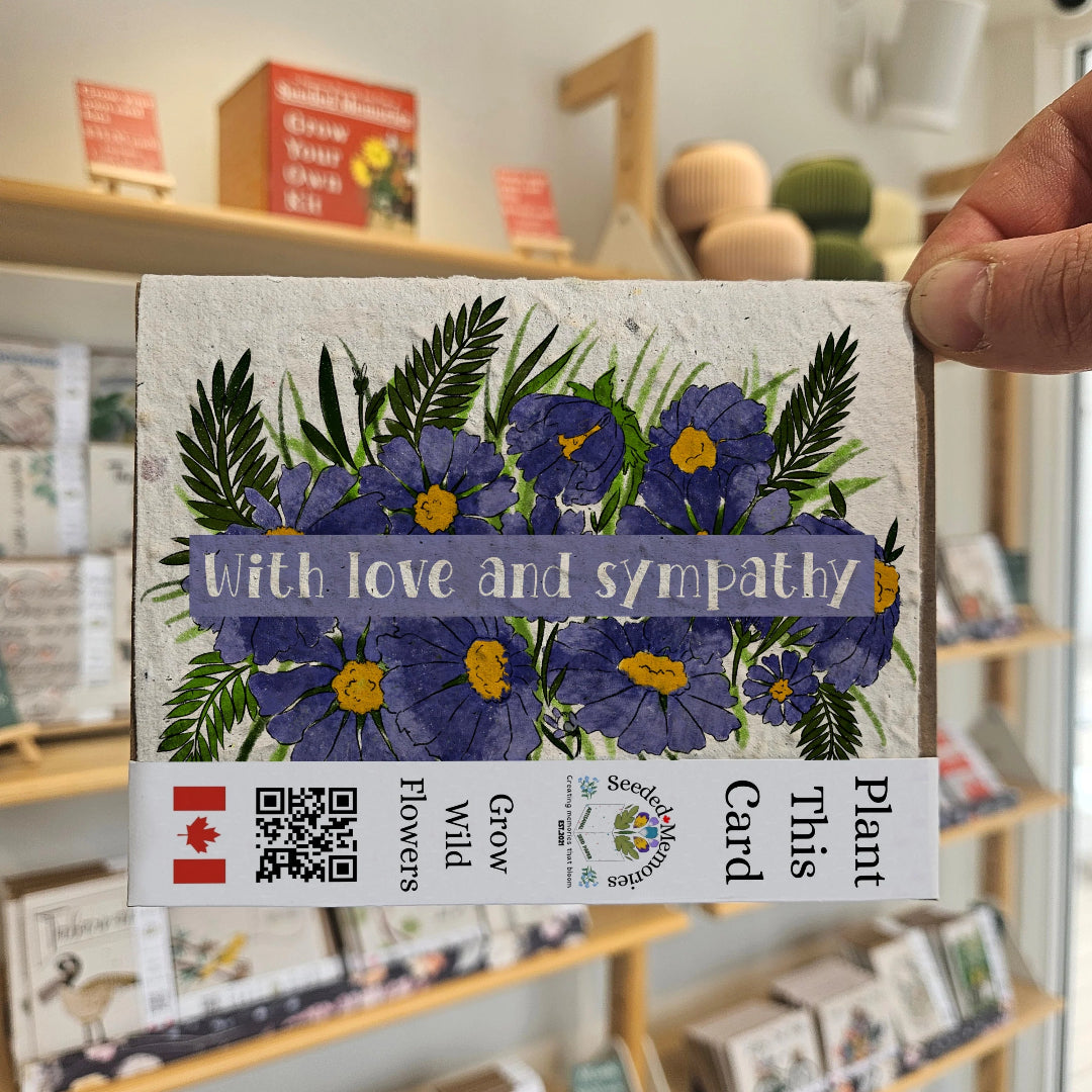 Plantable card with flowers and 'With love and sympathy' text, held in front of a store shelf.