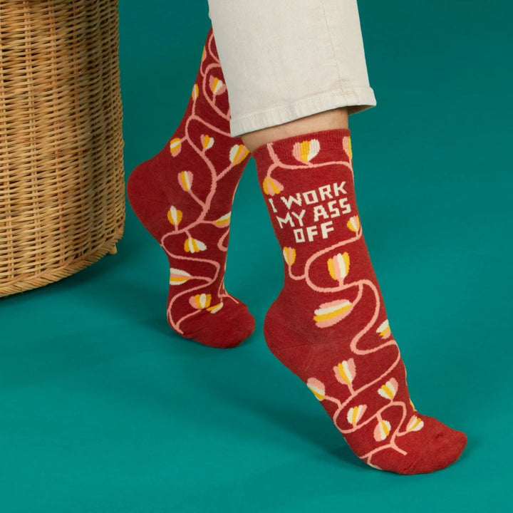 A pair of dark red women's crew socks with a winding vine pattern featuring yellow and pink tulip-shaped flowers. Text on one sock reads 