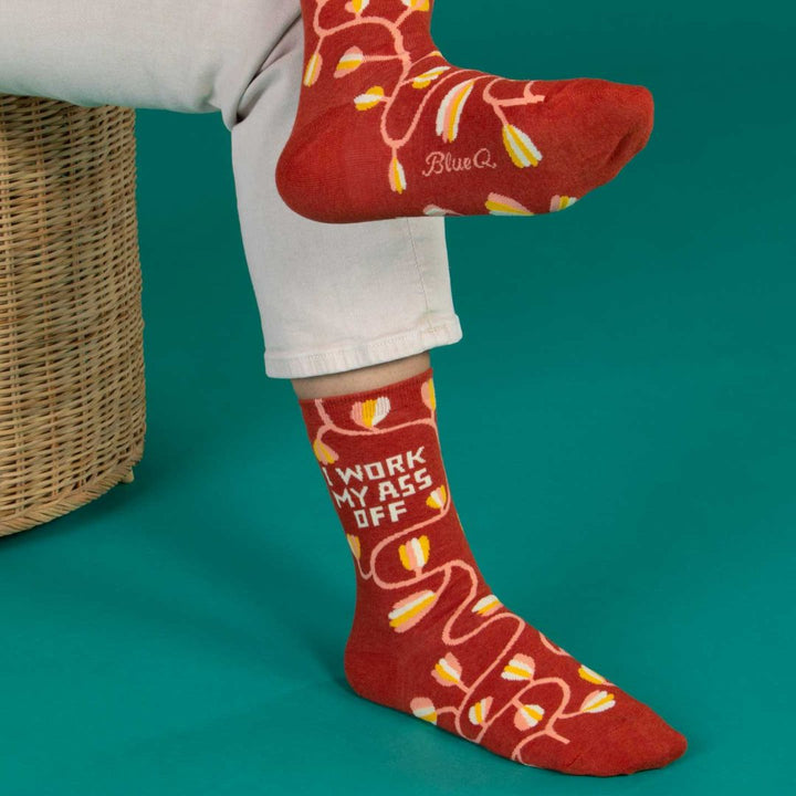 A pair of dark red women's crew socks with a winding vine pattern featuring yellow and pink tulip-shaped flowers. Text on one sock reads 
