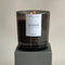 A black glass jar candle with a white label. The label reads 