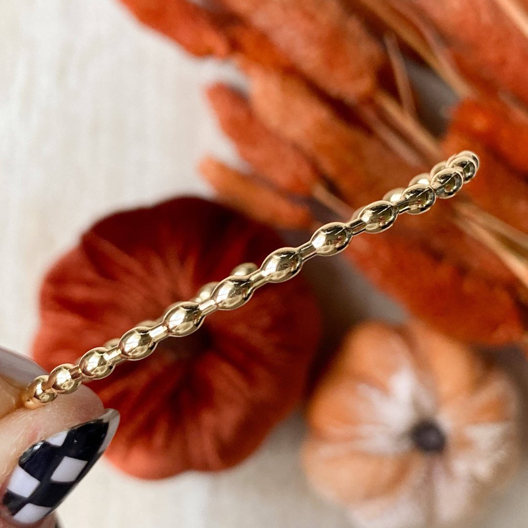 A gold-toned bangle bracelet with a row of small, rounded beads. 