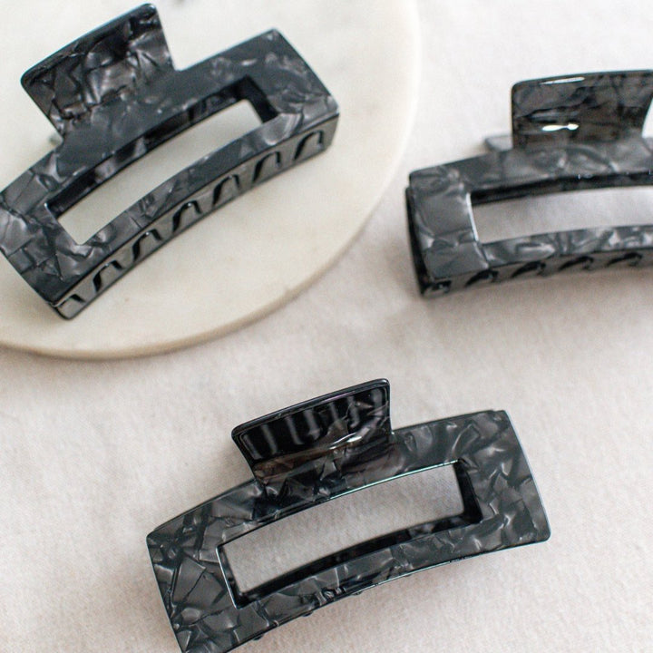 Three large hair claw clips in a black marble pattern on a white marble surface.