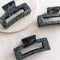 Three large hair claw clips in a black marble pattern on a white marble surface.