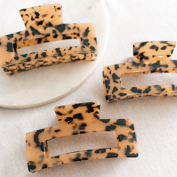 Three large hair claw clips in a leopard print pattern on a white marble surface.