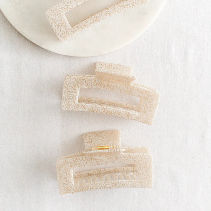 Three large hair claw clips in a light leopard print pattern on a white marble surface.
