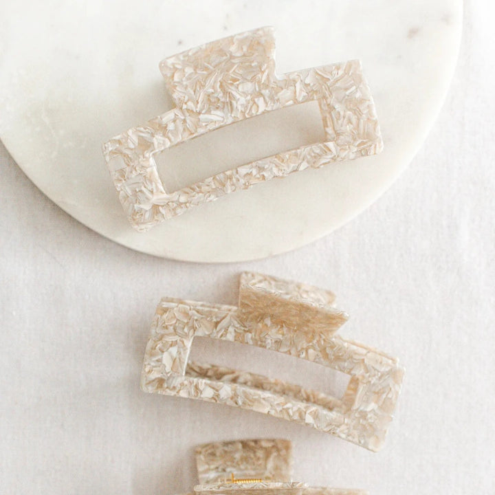 Three large hair claw clips in a light cream marble print pattern on a white marble surface.