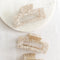 Three large hair claw clips in a light cream marble print pattern on a white marble surface.