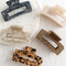 Four hair claw clips on a white marble surface. The clips are in various colors and patterns, including black marbled, beige marbled, brown and black leopard print, and a light brown marbled pattern.