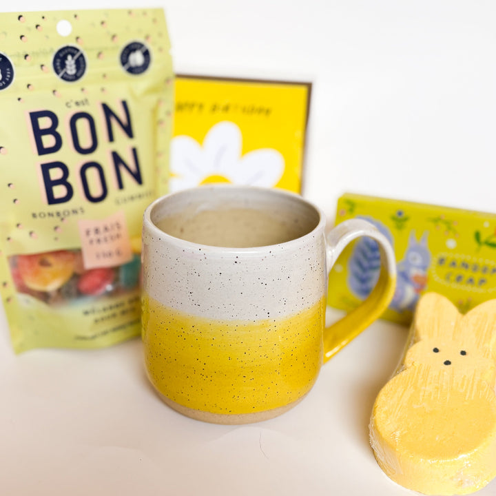 Yellow Dipped Mug by Valerie Daoust, a handmade ceramic mug with a colorblock design featuring a light gray top and a speckled yellow middle section, displayed on a light gray background. The mug has a large, rounded handle, a speckled texture, and is made in Mississippi Mills, Ontario, Canada.