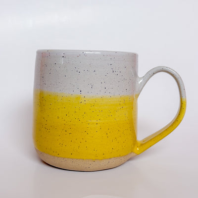 Yellow Dipped Mug by Valerie Daoust, a handmade ceramic mug with a colorblock design featuring a light gray top and a speckled yellow middle section, displayed on a light gray background. The mug has a large, rounded handle, a speckled texture, and is made in Mississippi Mills, Ontario, Canada.