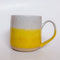 Yellow Dipped Mug by Valerie Daoust, a handmade ceramic mug with a colorblock design featuring a light gray top and a speckled yellow middle section, displayed on a light gray background. The mug has a large, rounded handle, a speckled texture, and is made in Mississippi Mills, Ontario, Canada.