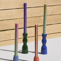 Four colorful taper candles in different colors and stripe patterns, displayed in matching sculptural holders against a light wood plank background.