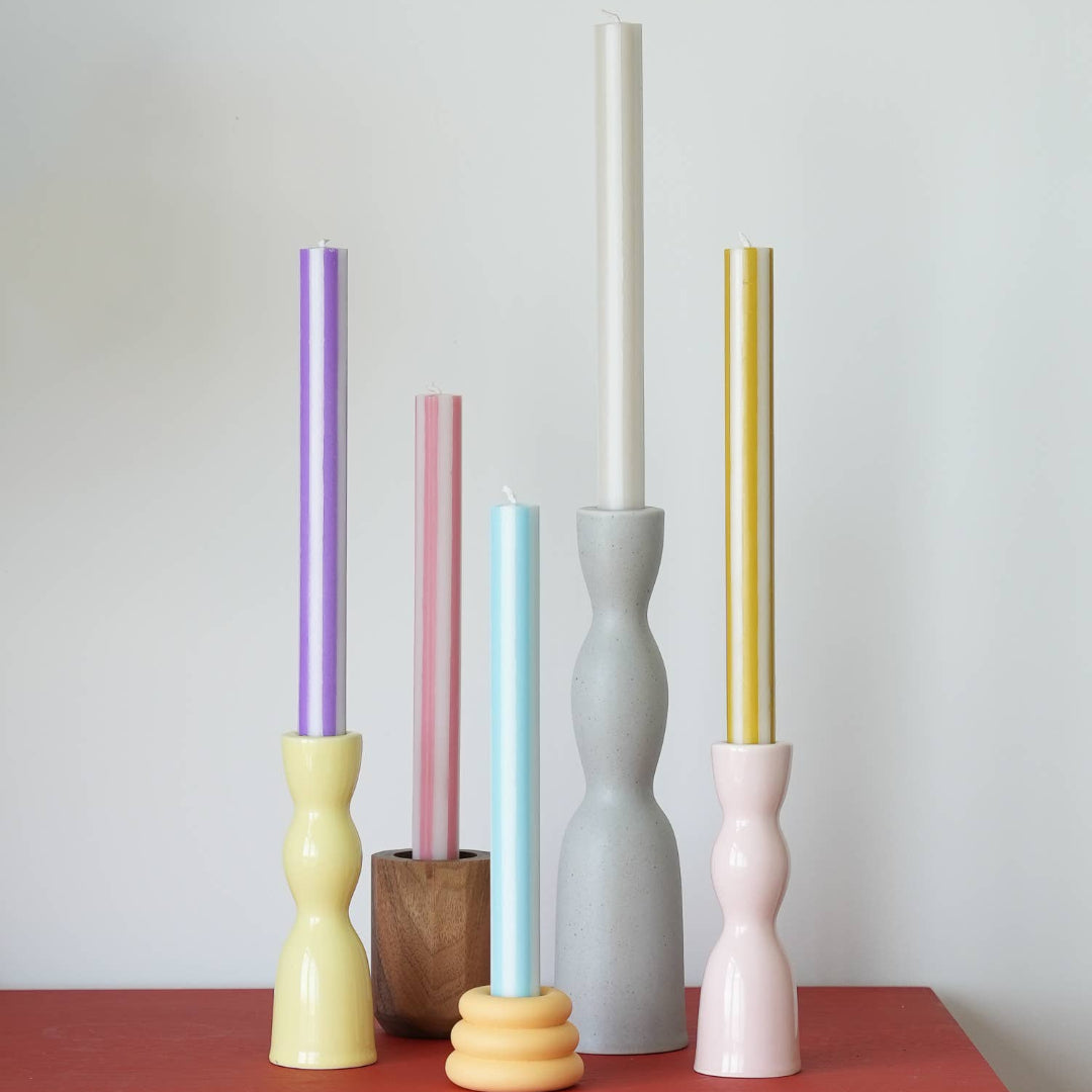 Colorful candles in various holders on a red surface with a white background