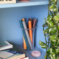 Colorful pencils in a clear cup on a blue shelf with books and decorative items.