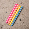Five striped candles in pink, orange, yellow, and blue, arranged diagonally on a textured concrete surface.