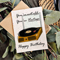 Birthday card with a turntable illustration and text on a leafy background