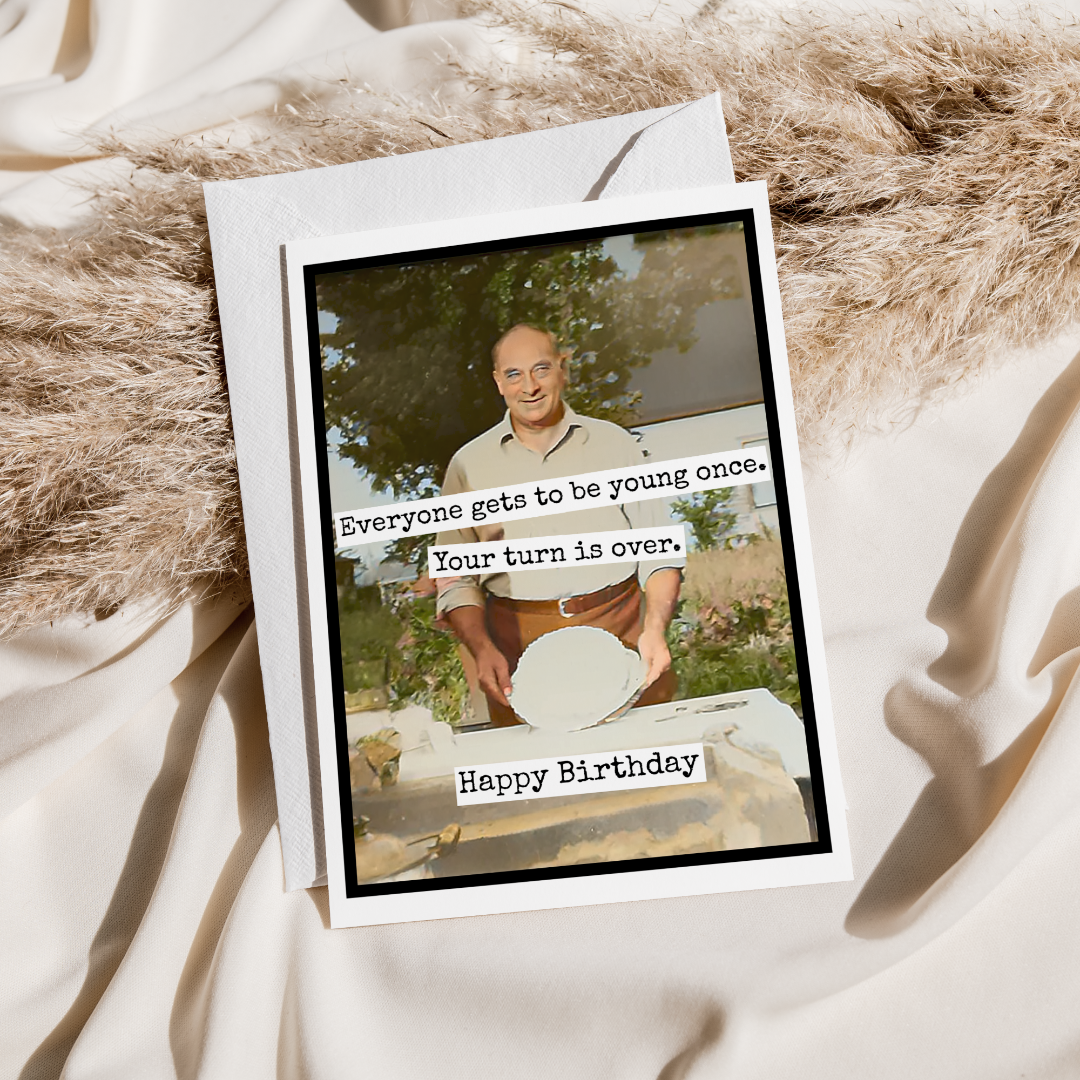 Birthday card with a humorous message and photo of a man, placed on a textured surface.