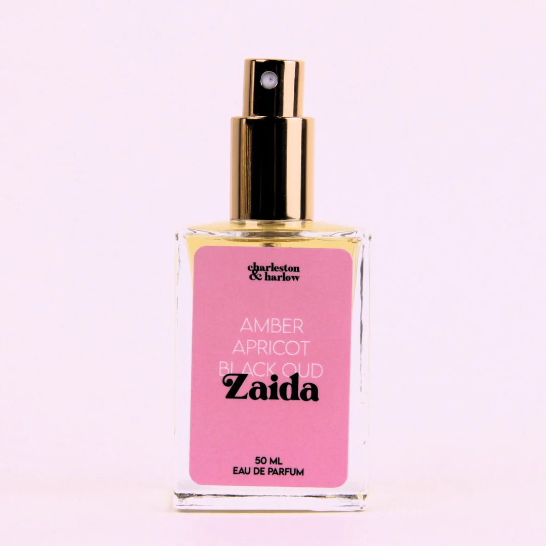 A bottle of Charleston & Harlow perfume named "Zaida." The bottle is clear glass with a gold spray cap. The label is pink with the brand name and perfume name in a bold, playful font. The fragrance notes are listed as "Amber, Apricot, Black Oud."