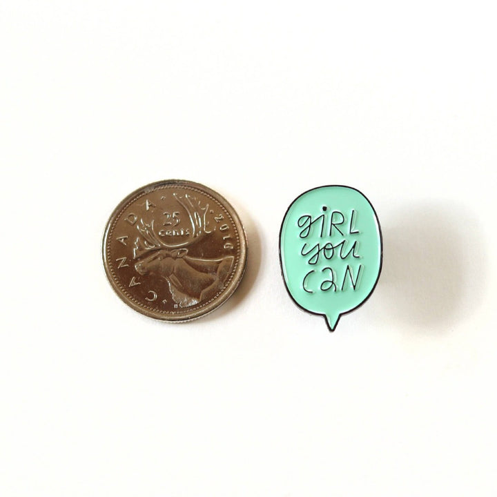 A mint green enamel pin in the shape of a speech bubble. The text 