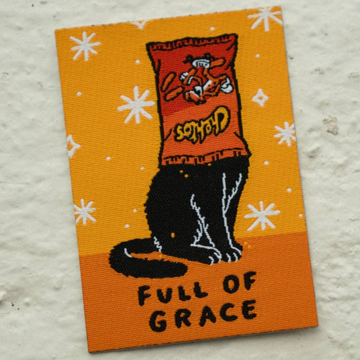  A black cat with a bag of Cheetos on its head is sitting upright. The cat is outlined in black and has a mischievous expression. The text 