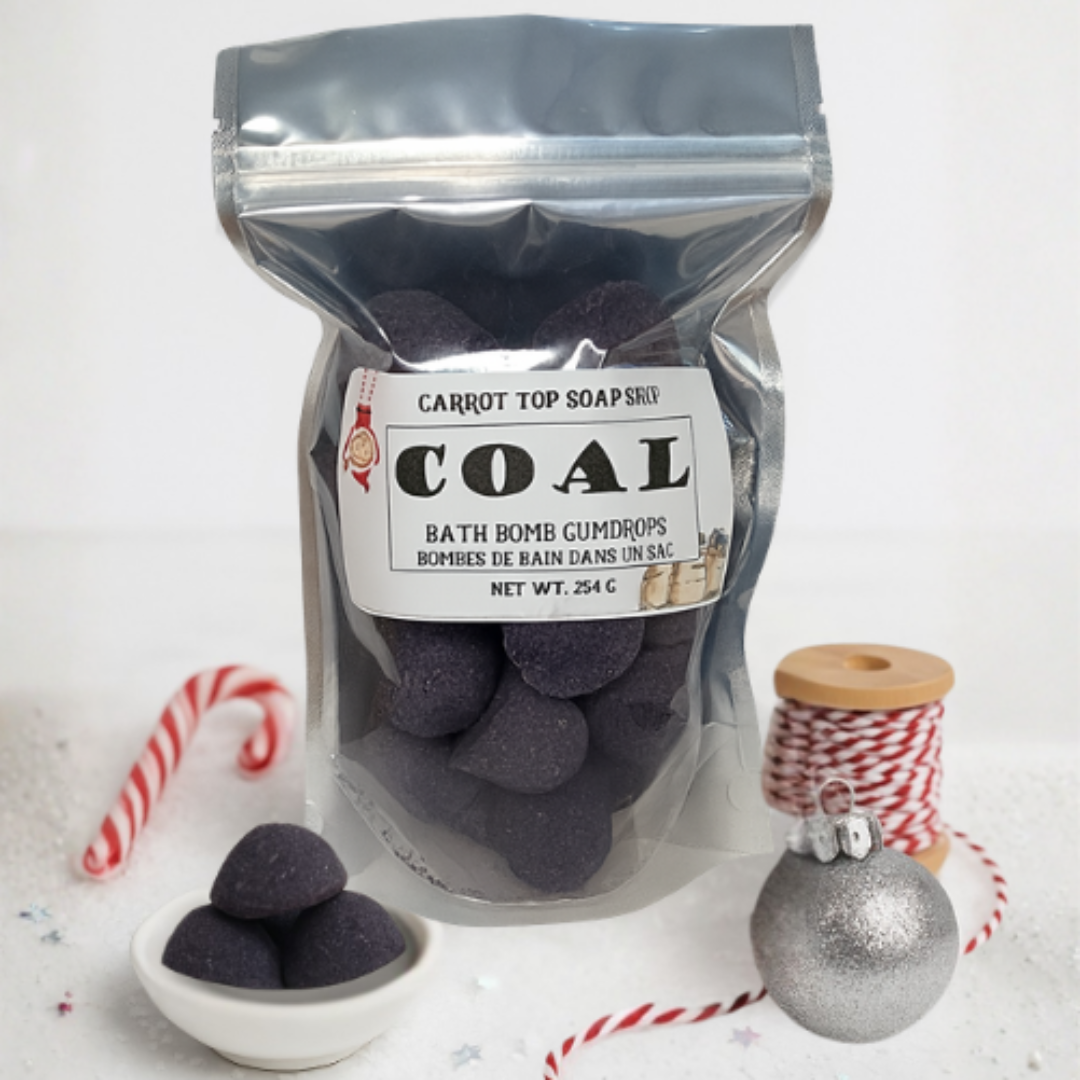 Bag of 'Coal' bath bomb gumdrops with a label, candy cane, and ornament on a white background