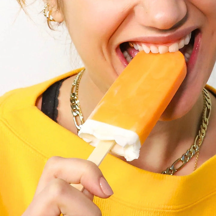 A person eatting a orange creamcicle popcicle.