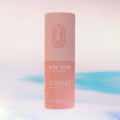 Sunset Glow Stick, a solid highlighter makeup stick in a warm coral pink sunset colour. It is presented in a cardboard tube, with a pull off top.