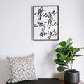 Framed wood sign with the text "These are the days" in black brush script against a white background.