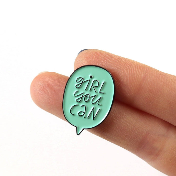 A mint green enamel pin in the shape of a speech bubble. The text 
